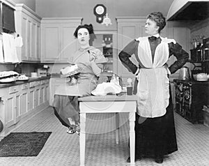 Housekeeper in the kitchen glaring at a young woman eating a cake