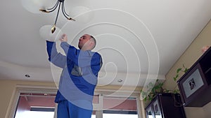 Housekeeper man climb up and change light bulbs in chandelier.