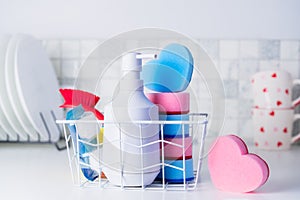 Housekeeping concept. Dish soap, heart shaped sponges, brush and pills in the basket on the background of clean plates