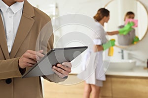 Housekeeping manager with tablet checking maid`s work in hotel bathroom, closeup