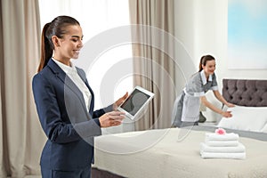 Housekeeping manager with tablet checking maid work in hotel room