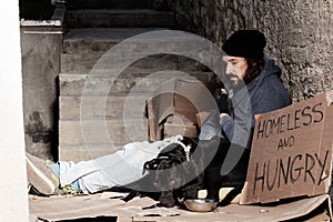 Houseless man sitting with his dog on backstreet