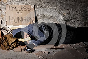 Houseless man sleeping on the street with alms box photo