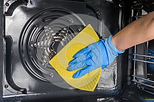 Housemaid in protective gloves washes an electric oven with a yellow rag