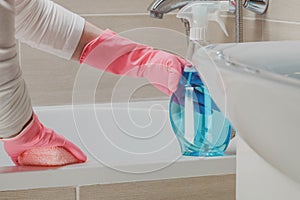 Housemaid in the rubber gloves cleaning bathroom with a sponge