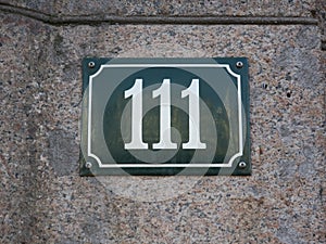 Housenumber 111 on an enamel sign on a stone wall