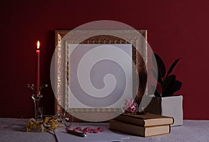 Houseplant, candlestick on a long leg with a burning candle, old books, old photo frame on a red background