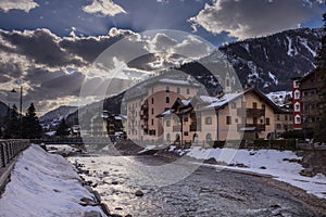 Houses and hotels in Moena, a city in italian Val di Fassa on a sunny winter day rising over the river in the centre