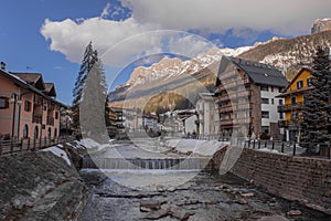 Houses and hotels in Moena, a city in italian Val di Fassa on a sunny winter day rising over the river in the centre