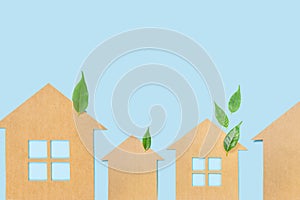 Houses made of craft paper and green leaves of a plant on a light blue background