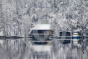 Houses near the frozen river covered with snow and surrounded by forest