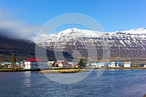 Houses in sea harbor of Norther Iceland with snowy mountains nearby.
