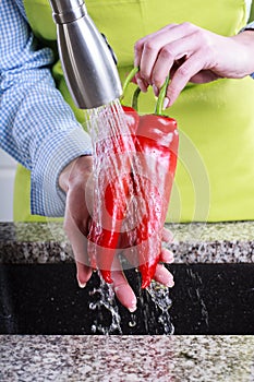 Housewife in apron washing red peppers