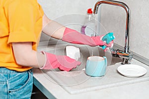 A housewife in casual clothes and pink rubber gloves is squeezes the sponge. Close up of hands