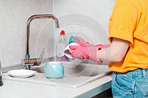 A housewife in casual clothes and pink rubber gloves is washing a cup. Close up of hands