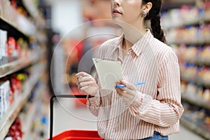 Housewife choosing groceries in supermarket. Millennial young woman holding list of products is shopping. Close up. In