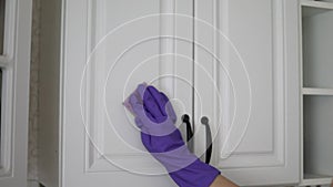Housewife cleans doors of wooden kitchen with sponge in purple gloves closet at home backside view