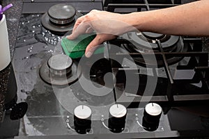 A housewife cleans the kitchen gas glass-ceramic black stove with a sponge. House cleaning