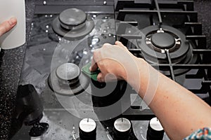 A housewife cleans the kitchen gas stove with a sponge. Maintenance of tempered glass and glass ceramics