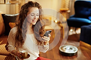 Housewife with coffee cup using smart home app and robot vacuum