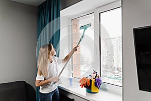 Housewife is doing chores and washing windows indoor in apartment. Windows cleaning service. Woman cleaner with mop is