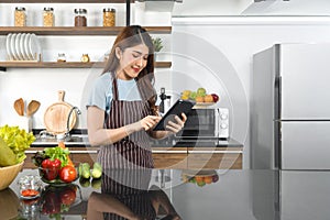 The housewife dressed in an apron  using tablet computer to find recipes on the internet. Morning atmosphere in a modern kitchen