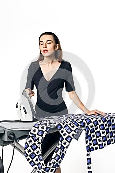 Housewife fatal woman in a black dress ironing things, blowing on a burnt finger. Isolated on a white background