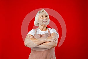 Housewife female chef cook confectioner or baker in apron standing on red background in studio. Crossed arms.