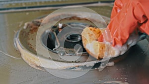 Housewife in gloves washes the dirty surface of a gas stove with a washcloth