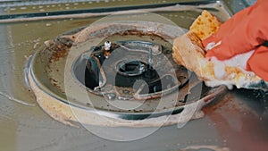 Housewife in gloves washes the dirty surface of a gas stove with a washcloth