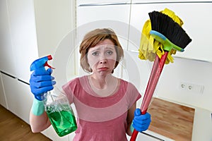 Housewife at home kitchen in gloves holding cleaning broom and mop and spray bottle