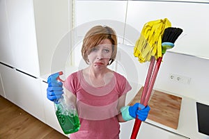 Housewife at home kitchen in gloves holding cleaning broom and mop and spray bottle