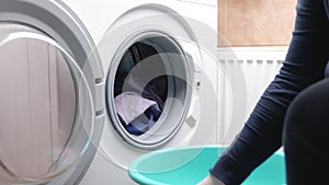 Housewife loads clothes from Laundry basket into a washing machine