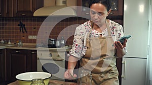 Housewife looks through the phone, prepares canned cucumbers according to a recipe from the Internet, in a home kitchen.