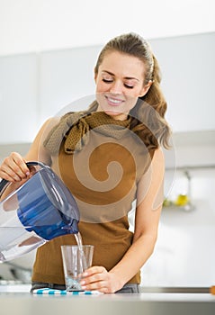 Housewife pouring water into glass from water filter pitcher