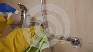 A housewife in protective rubber yellow gloves cleans a stainless steel faucet with a washing gel. Dirty bathroom faucet