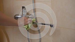 A housewife in protective rubber yellow gloves cleans a stainless steel faucet with a washing gel. Dirty bathroom faucet