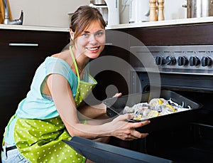 Housewife putting tray with fish in oven