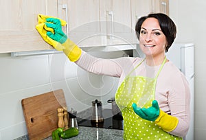 Housewife removing spots from cupboards in kitchen
