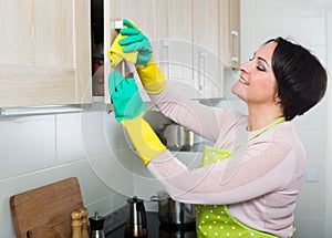 Housewife removing spots from cupboards in kitchen