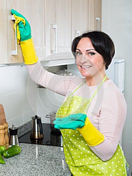 Housewife removing spots from cupboards in kitchen