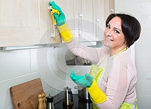 Housewife removing spots from cupboards in kitchen