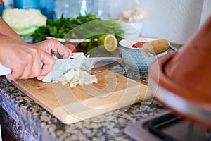 Housewife& x27;s hands slicing and chopping onion on wooden cutting board, preparing a healthy salad for dinner at home.