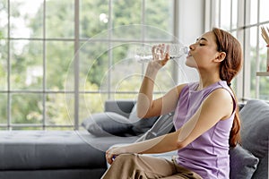 Housewife sitting on sofa and drinking mineral water in plastic bottles