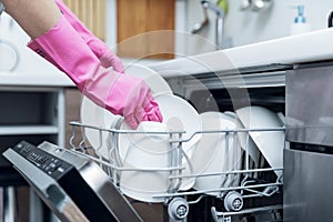 housewife taking out clean dishware from dishwasher at home kitchen