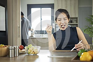 Housewife using digital tablet and eating fresh organic vegetarian salad in home kitchen.