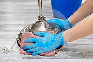 housewife wearing gloves wipes a floor lamp with a rag.