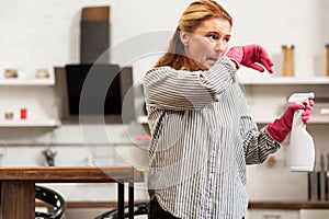 Housewife wearing shirt and gloves cleaning her flat and sneezing