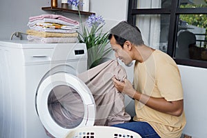 Housework. asian Man loading clothes into washing machine