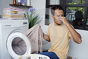 Housework. asian Man loading clothes into washing machine smell badly